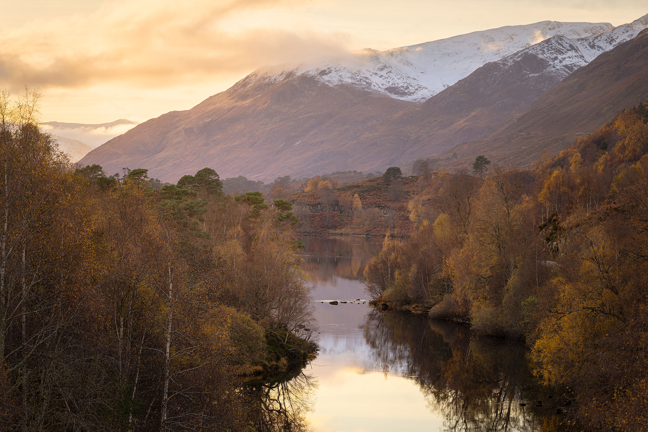 A pastel sunset frames the autumn trees and mountains in Glen Affric, Scotland
