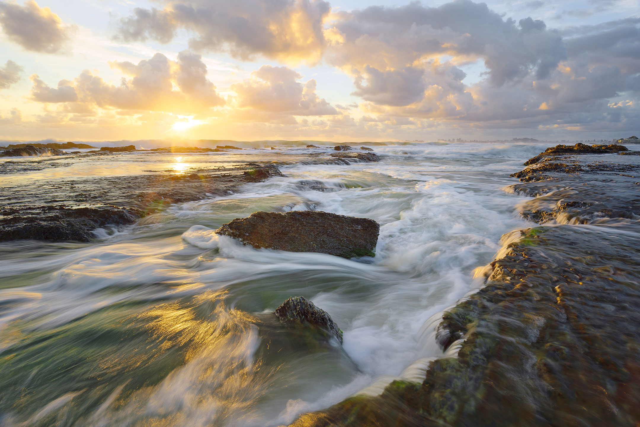 The early morning sun breaking through the clouds over the ocean and rocks at Currumbin Beach, Gold Coast, Australia